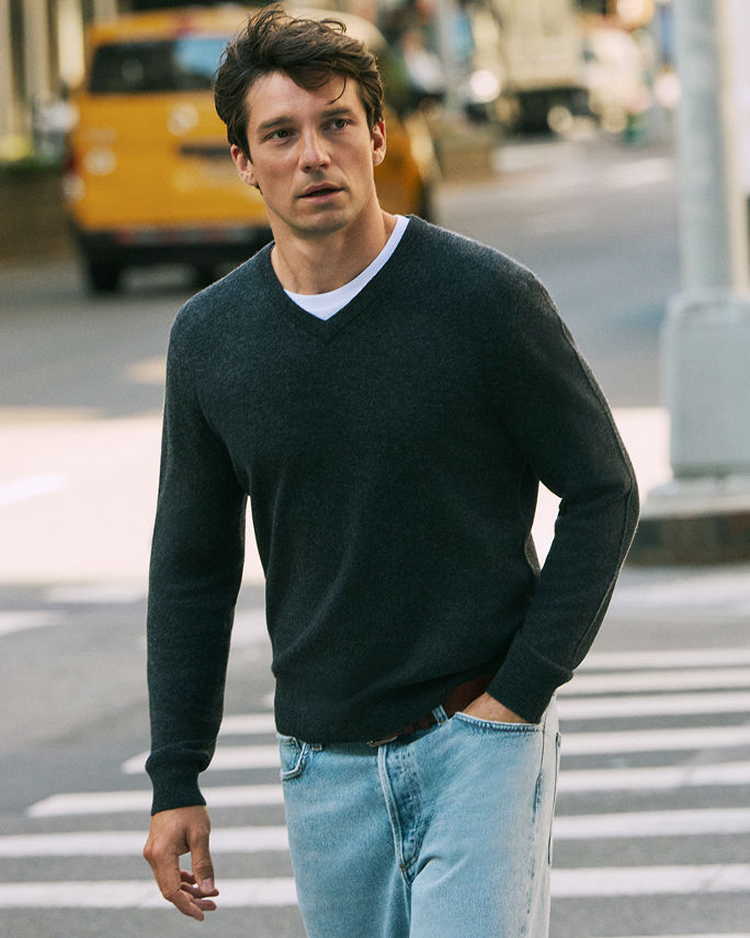 A man in a dark green V neck sweater and blue jeans. Elevate the everyday. Shop shirts & sweaters.