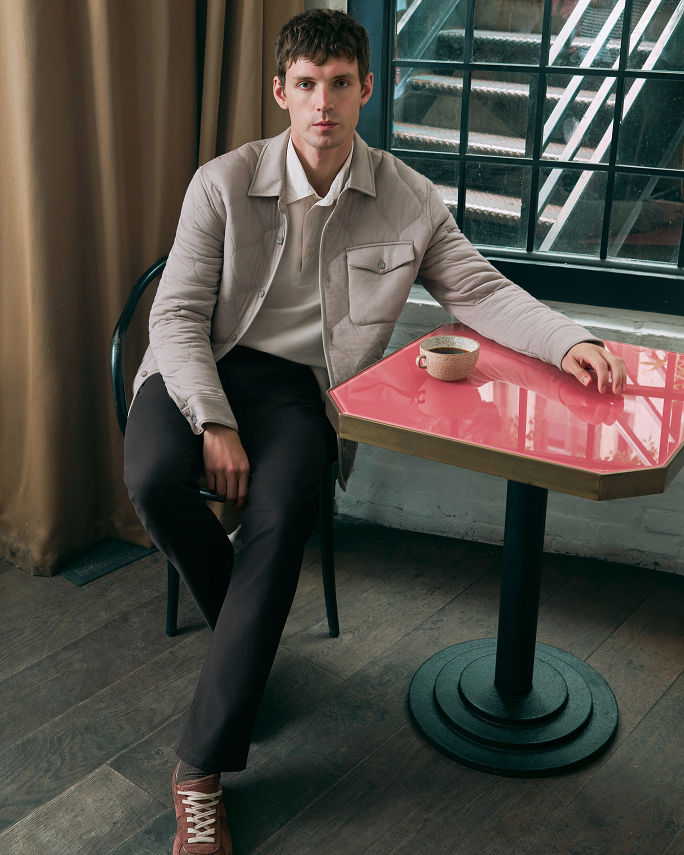 A man in a quilted shirt jacket and dark trousers. Elevate the everyday. Shop pants.
