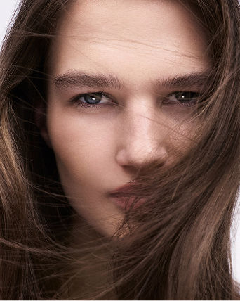 A womans face with her brown hair blowing in her face. Featured shops, hair care.