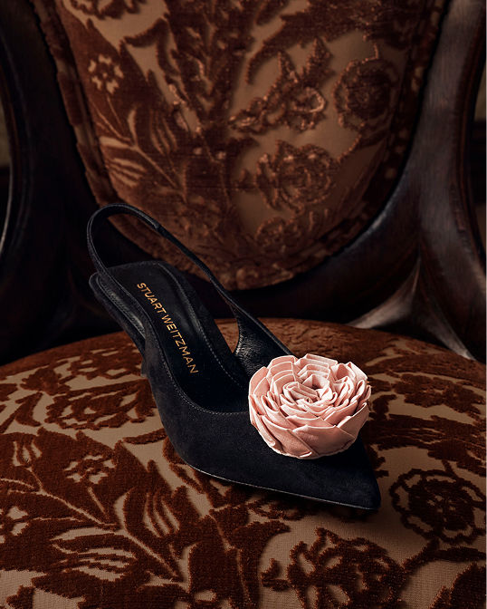 A single black Stuart Weitzman slingback pump with a large pink flower embellishment. Shop embellished accessories.