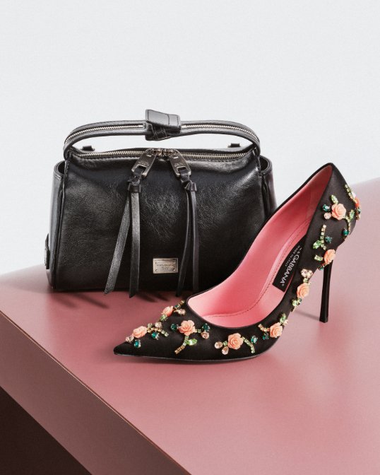 A mini black leather Dolce and Gabbana handbag next to a floral embellished black high heel.
