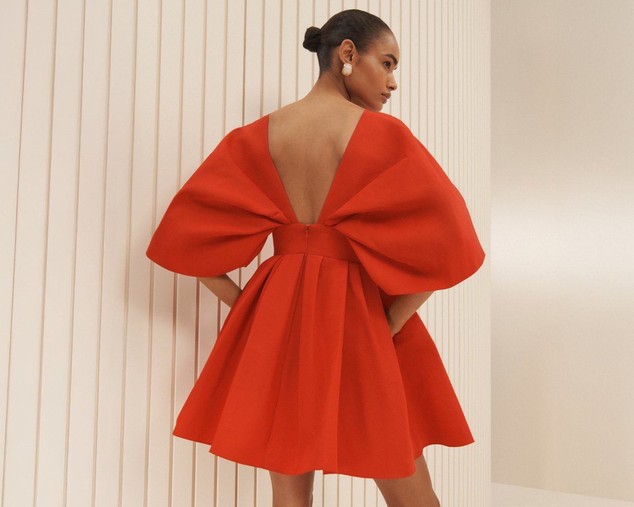 A woman from the back in a red Carolina Herrera mini dress with a flared skirt and sculptural sleeves.
