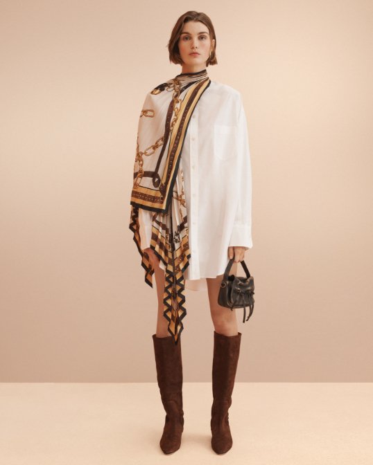 A female model in Acne Studios layered shirt dress and holding brown Acne Studios mini handbag.