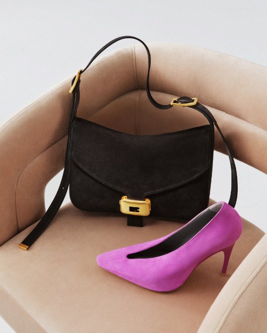 A black square Balenciaga handbag with gold details next to a fuchsia suede heel.