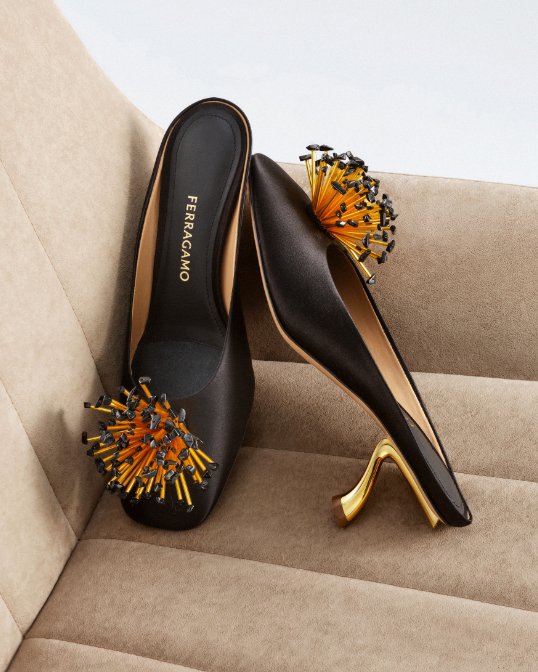 A pair of black Ferragamo kitten heels with a gold heel and orange burst embellishment on the toes.