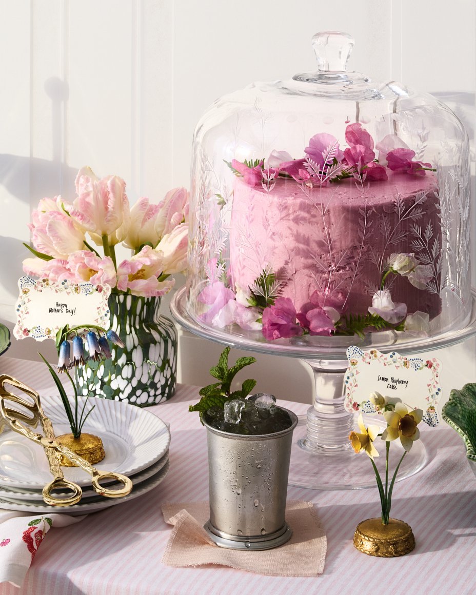 A pink striped table with a floral etched cake stand with pink layer cake, porcelain plates and flowers. Shop Easter.