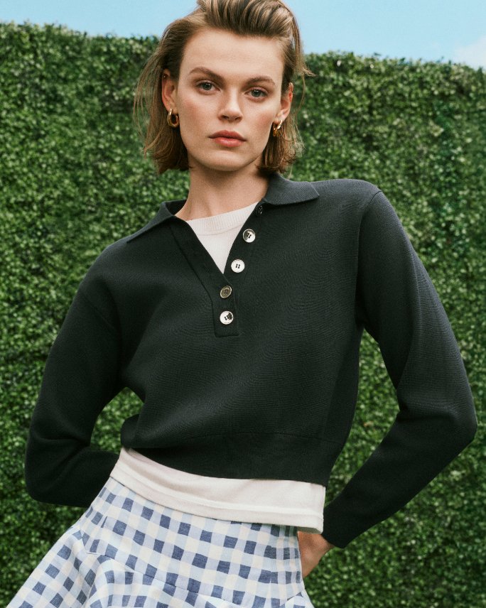 A woman in a long sleeve black polo and blue checked mini skirt. Shop polos and rugbys.