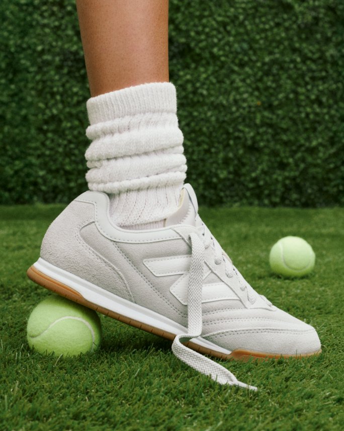 Closeup of a white New Balance sneaker stepping on a tennis ball on the grass. Shop slim sneakers.