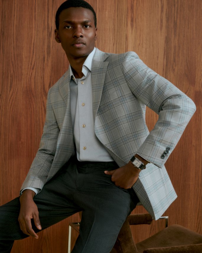 A man in a casual gray blazer, blue shirt & black pants. Explore the guides, mens suiting.