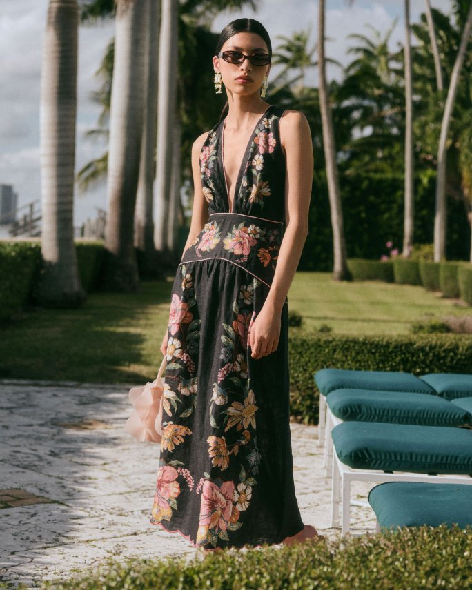 A woman in a tropical setting in a black floral sleeveless V neck dress. Explore the guides, well dressed guests.