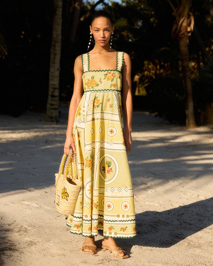 A woman in a yellow print long sundress on the beach.