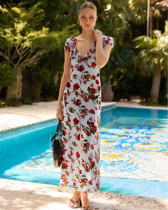 A woman next to a pool in a V neck blue with red printed flowers midi dress.