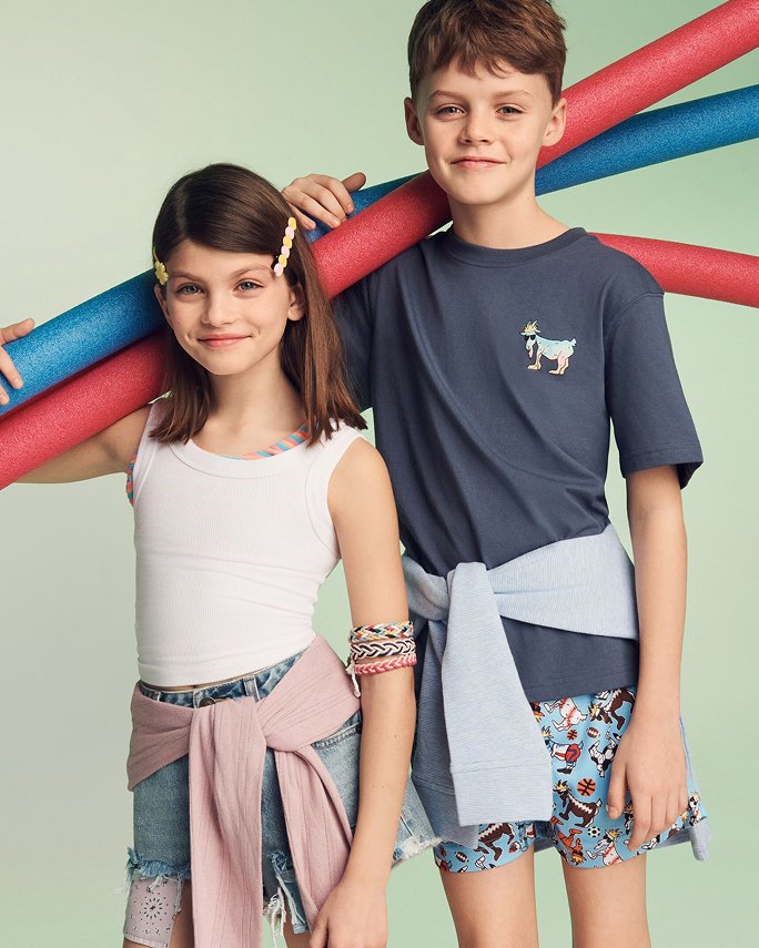A young boy and girl in summery shorts and tees, carrying pool floats. The camp shop.
