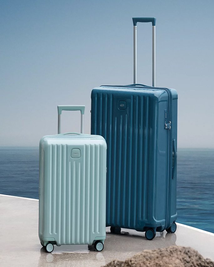 A dark blue hardcase luggage piece next to a smaller light blue carry on. Beach bound, luggage.