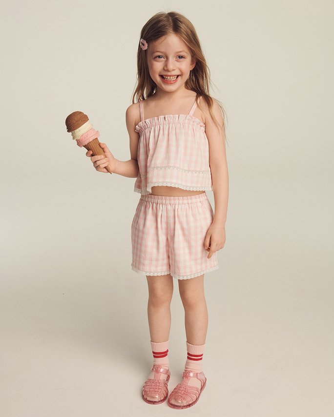 A young girl in a pink gingham top & matching shorts holding an ice cream cone. The camp shop.