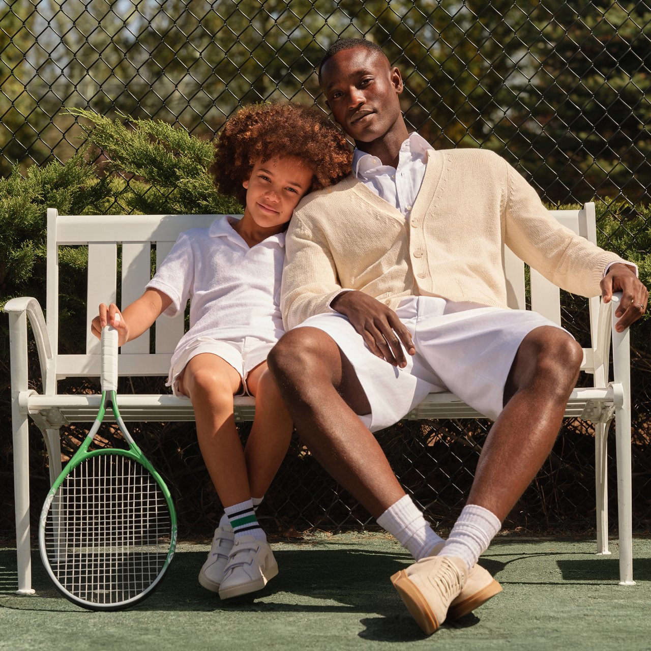 A man in a Boss and Beckham cream sweater, white shirt & shorts sitting next to a young boy.