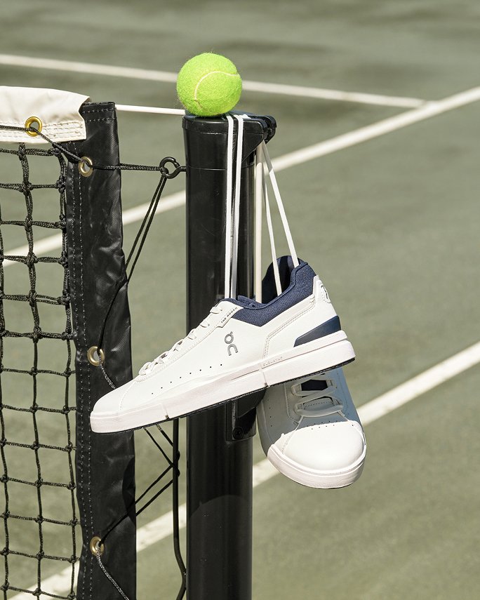 A pair of white On sneakers with blue trim hanging on end of a tennis net.
