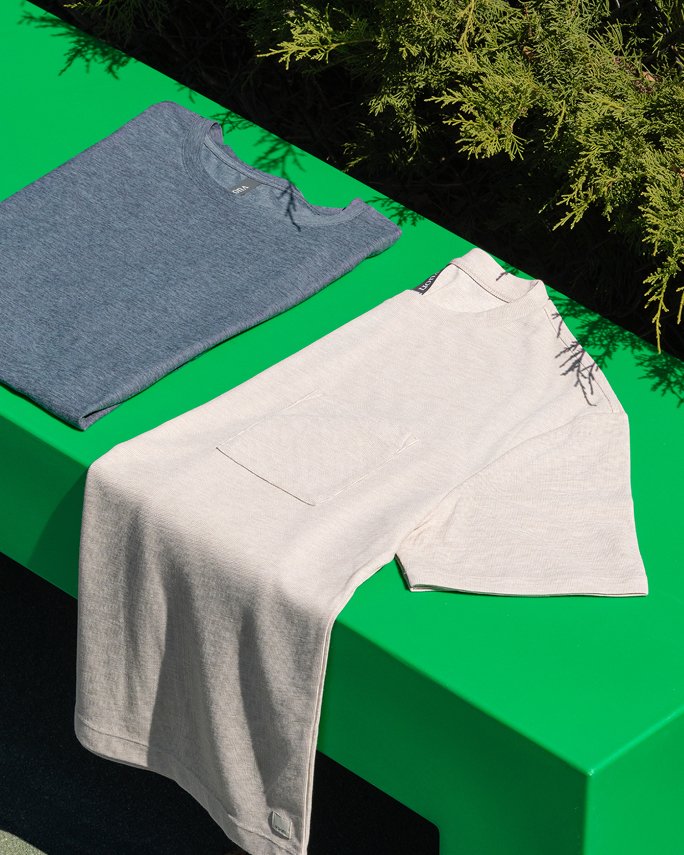 A folded blue Vuori tee next to a half folded white Vuori tee.