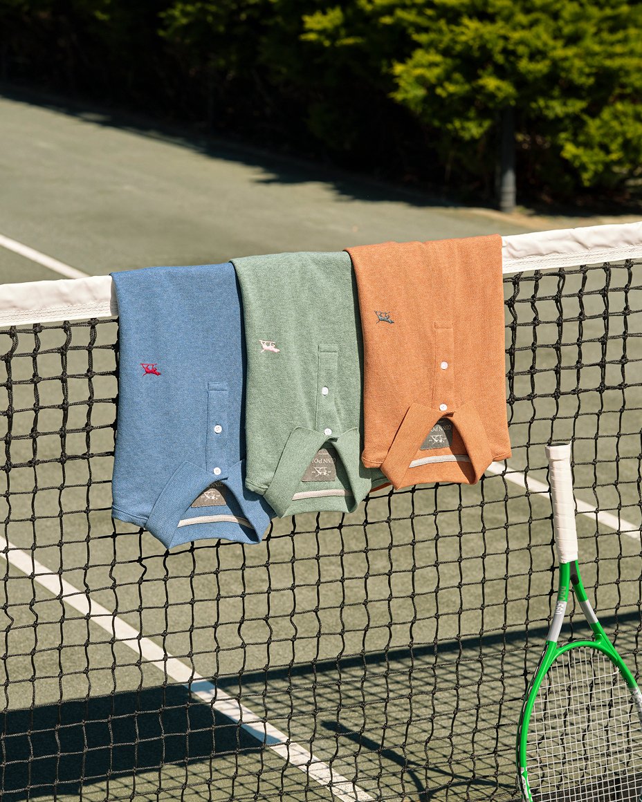 3 folded polos in blue, green & orange draped over a tennis net. Fathers Day gifts, gifts under $100.