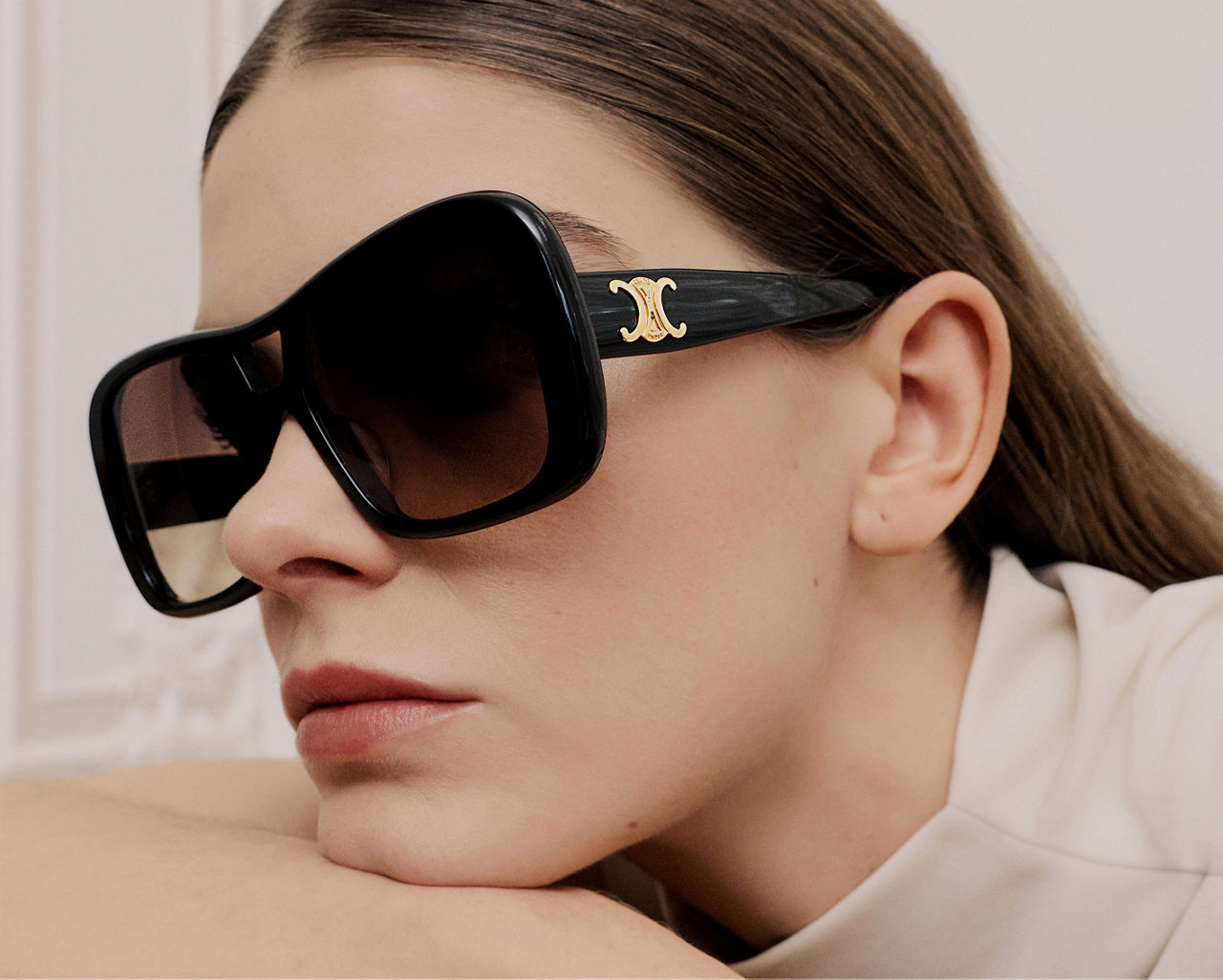 A woman resting her chin on her arm, wearing large Celine sunglasses. Statement eyewear, Celine.