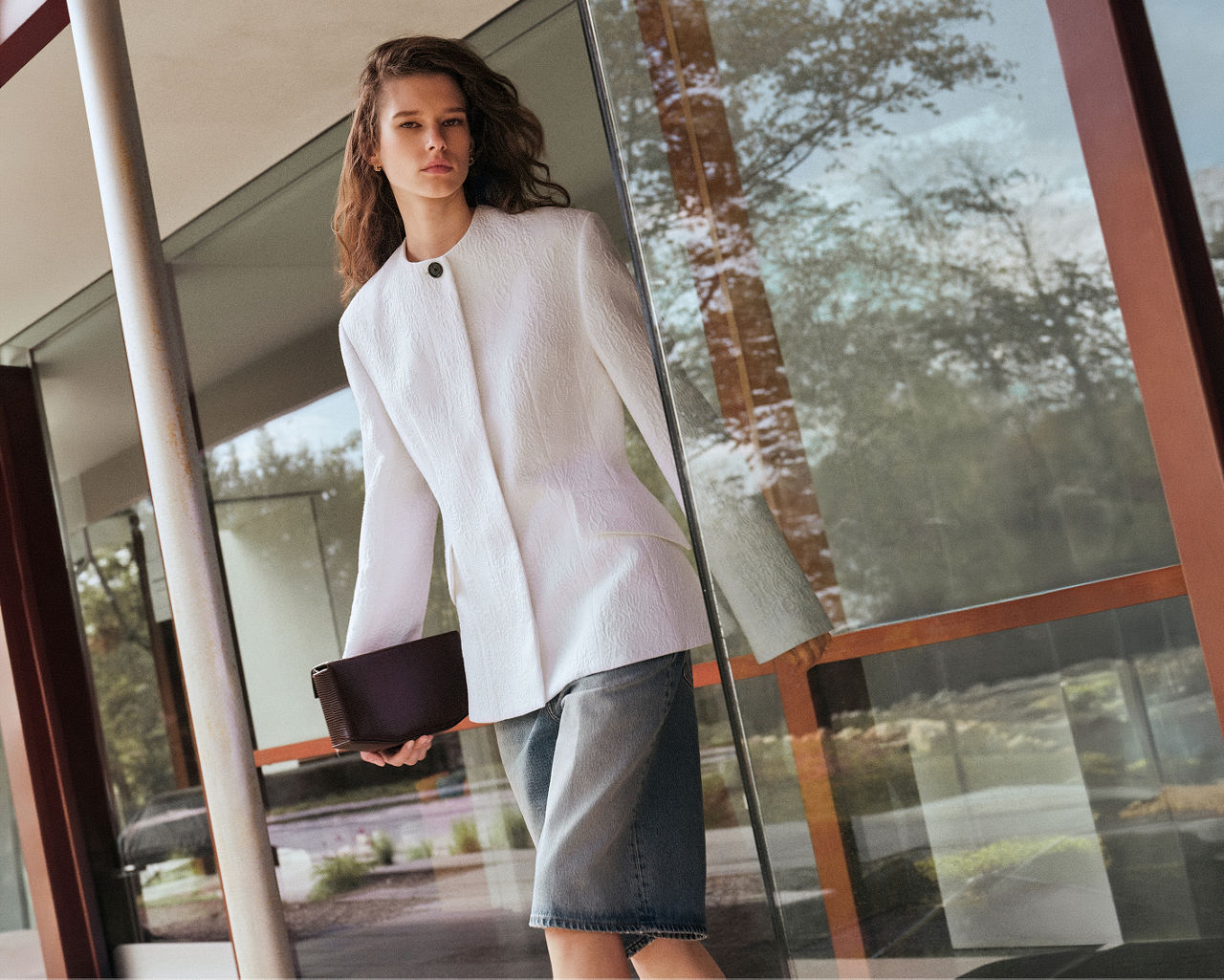 A woman in a structured white long sleeve top & denim skirt. The designer boutique, women.