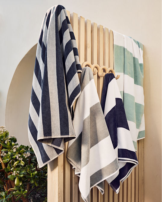 Striped towels hanging from a wooden fence. Shop bedding and bath.