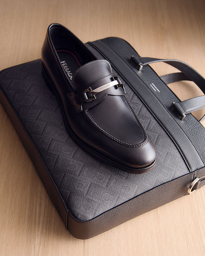 A single black loafer on top of a black briefcase. What to wear where, the office.