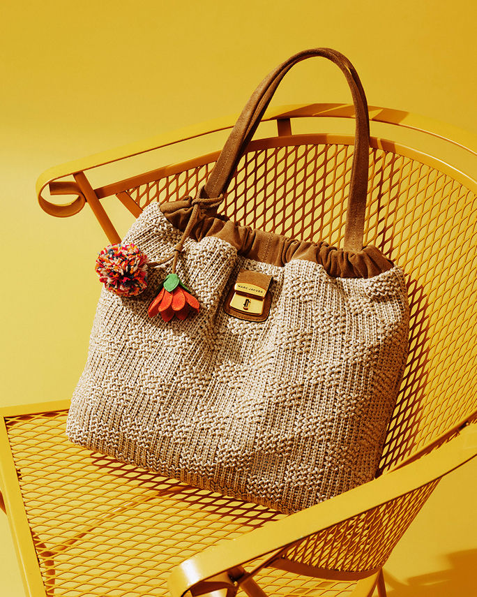 A brown canvas handbag with a flower charm and pompom charm. What to wear where, vacation.