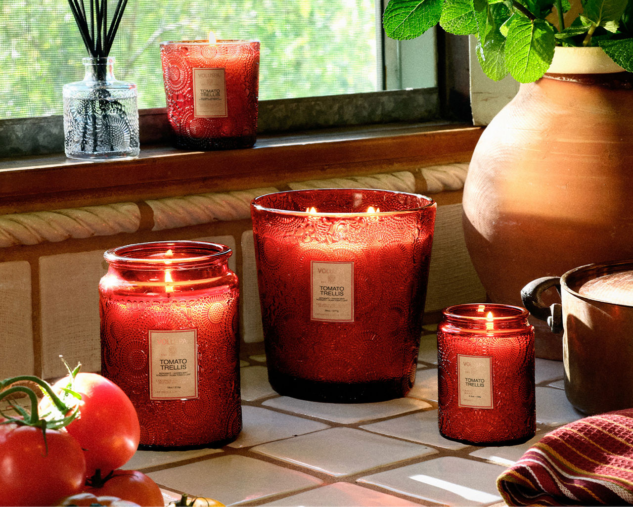 A variety of red Voluspa lit candles on a kitchen counter. New home arrivals. Shop Voluspa.
