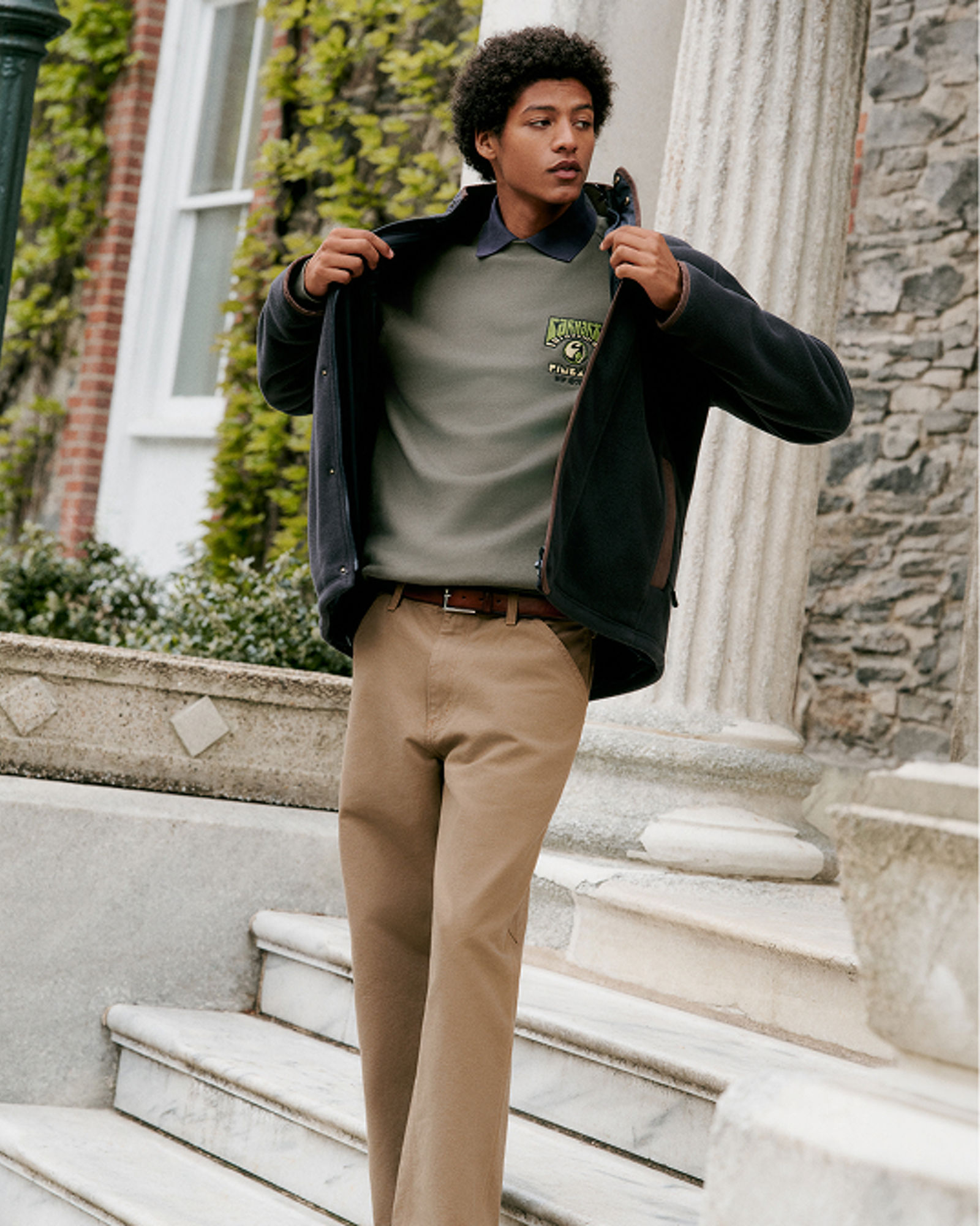 A man in a dark barn jacket over a sweater and brown jeans. Get ready for fall. Shop mens jackets. 