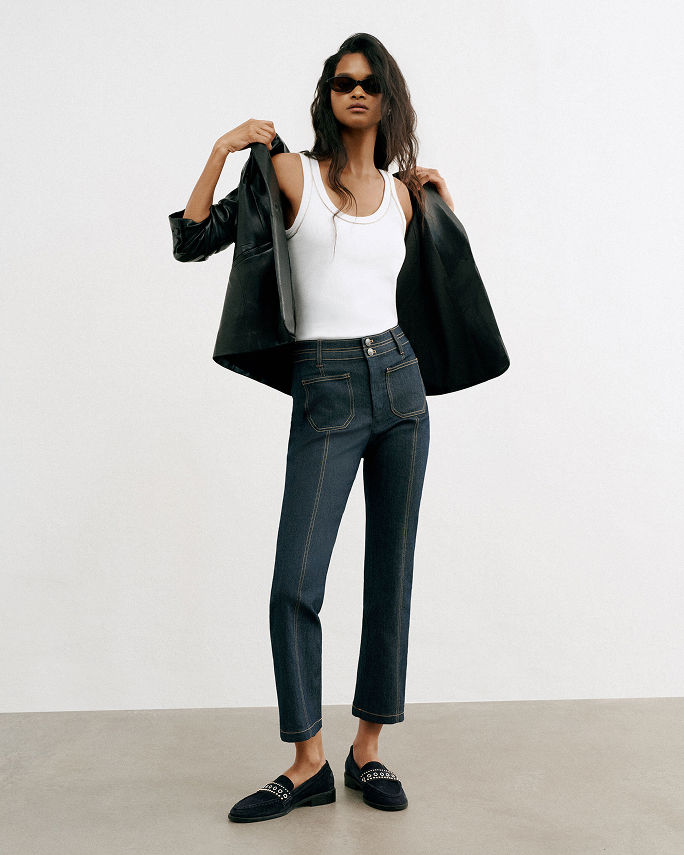 A woman in dark Cinq a Sept jeans, white tank top & black leather jacket. Denim labels we love, Cinq a Sept.