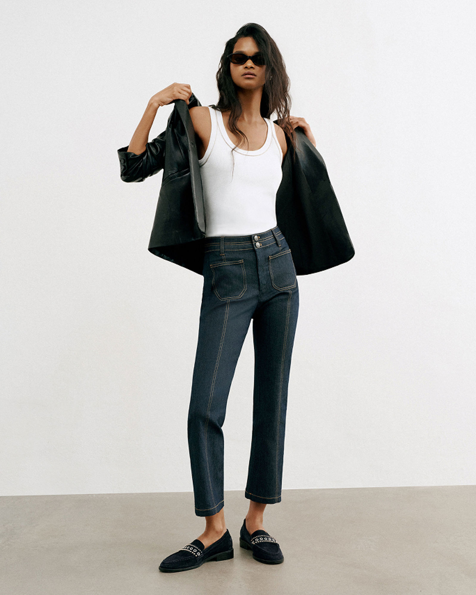 A woman in dark Cinq a Sept jeans, white tank top & black leather jacket. Denim labels we love, Cinq a Sept.