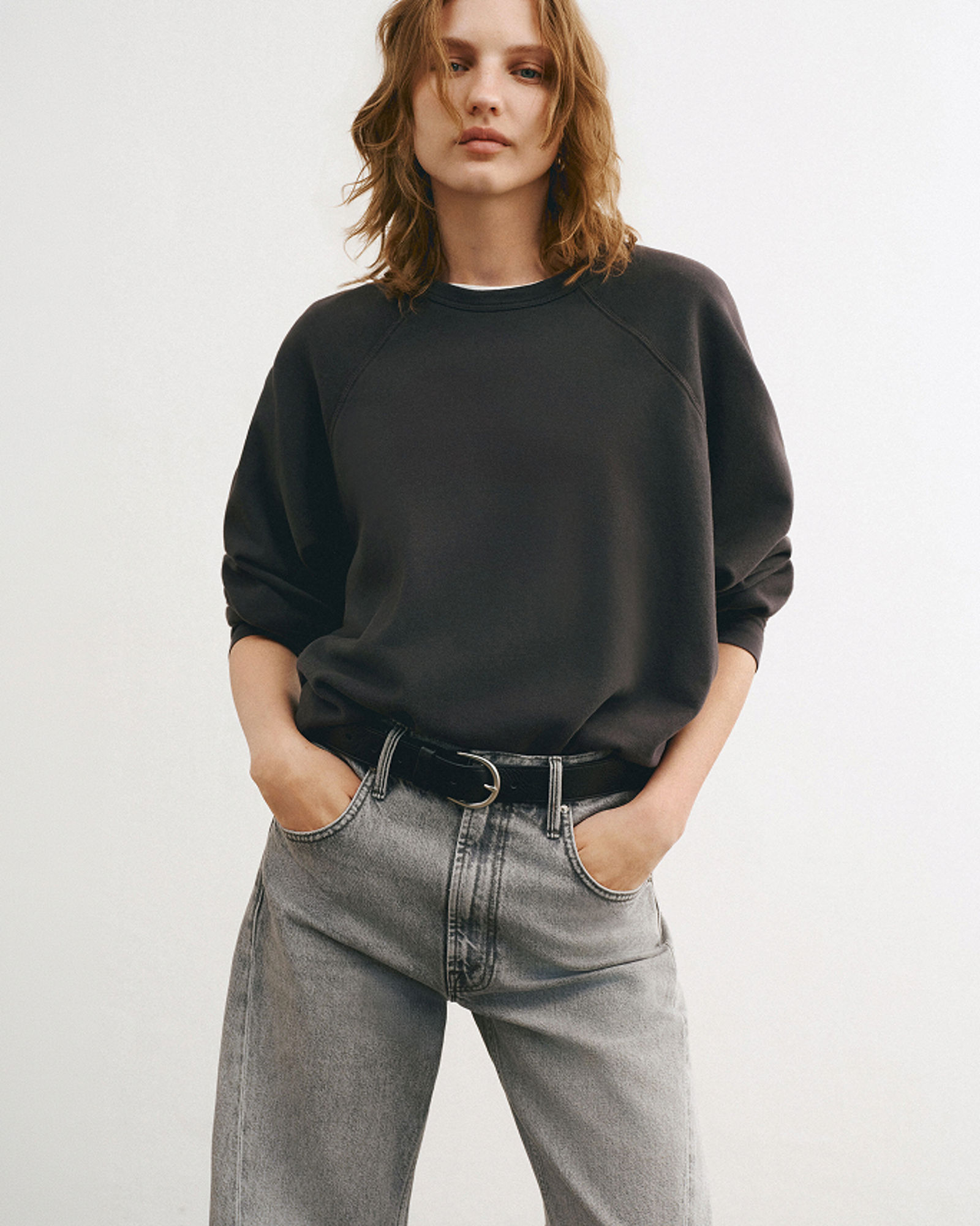 A woman in gray Mother jeans & black sweatshirt. Denim labels we love, Mother.