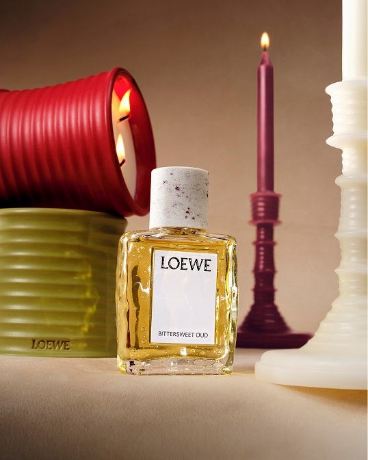 A bottle of Loewe fragrance and lit Loewe candles & candlesticks. Shop beauty.