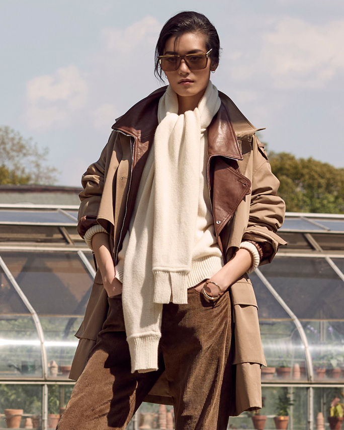 A woman in a brown trench coat layered over a brown leather bomber over a cream sweater. Shop heritage outerwear.
