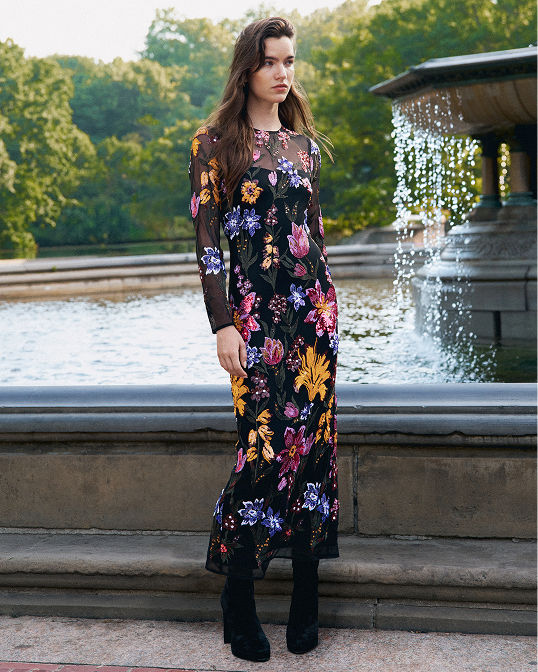 A woman in a long sleeve long dress with colorful embroidered flowers. Shop dresses.