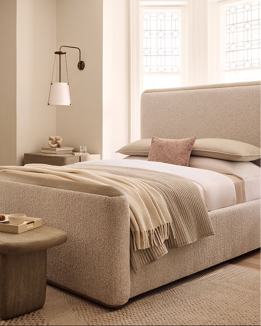 An upholstered bed made up with cream linens. Shop furniture and mattresses.