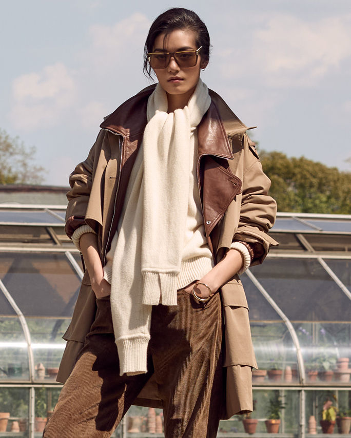 A woman in a brown trench coat layered over a brown leather bomber over a cream sweater. Shop heritage outerwear.$$