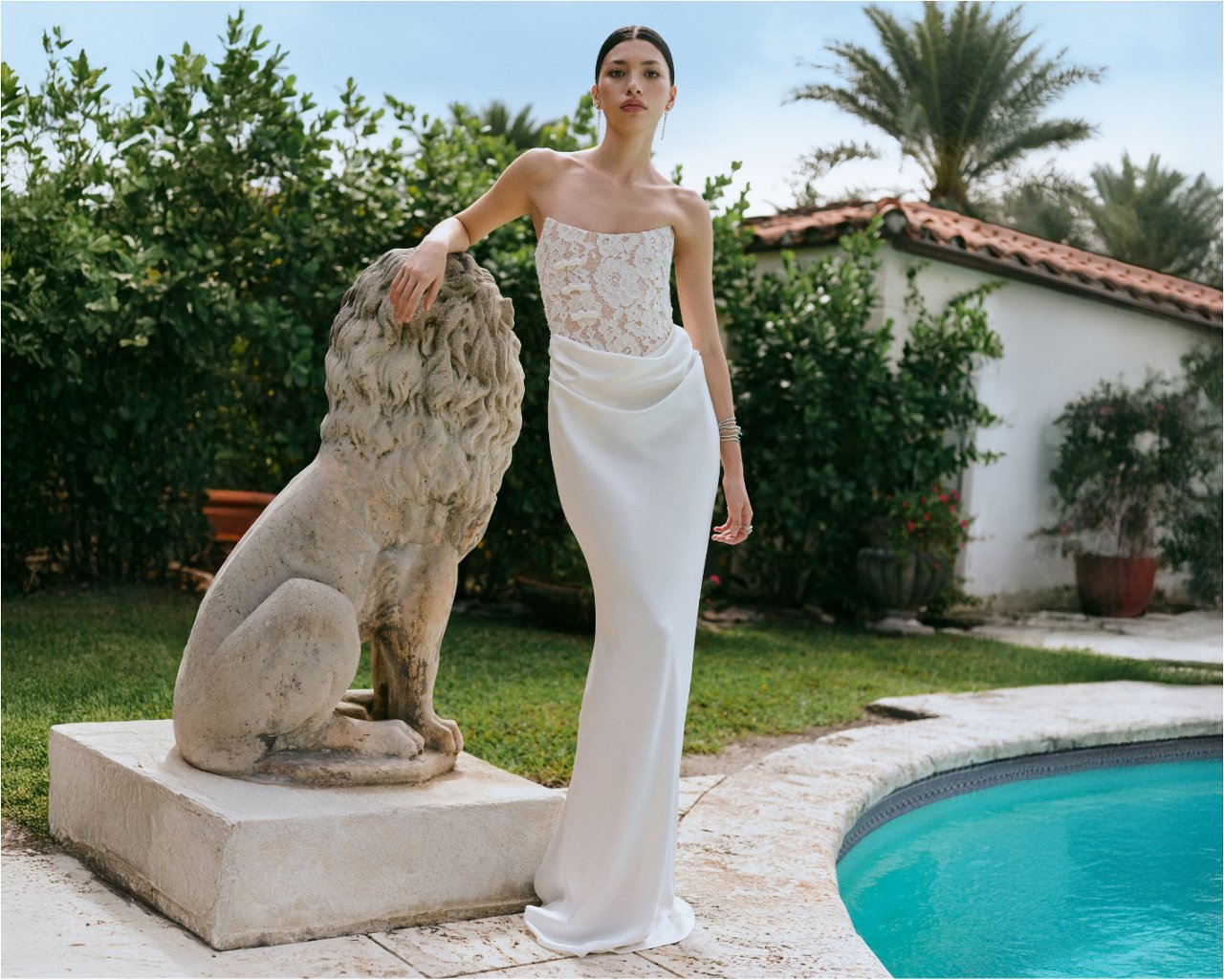 Woman next to a stone lion & a pool in a white strapless Sau Lee bridal dress with embroidered top.