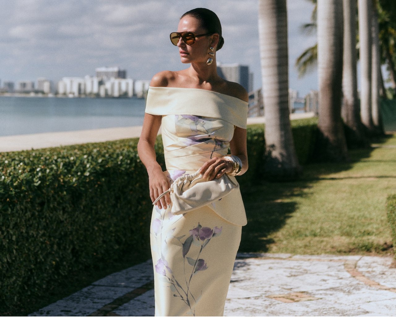 Woman in an off the shoulder yellow cocktail dress with purple printed flowers.