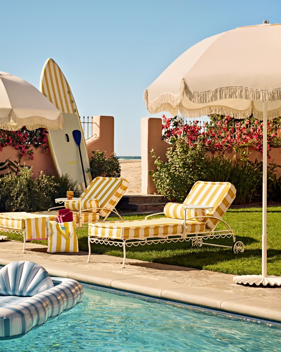 Yellow & white striped loungers and a large beach umbrella on a lawn next to a pool.