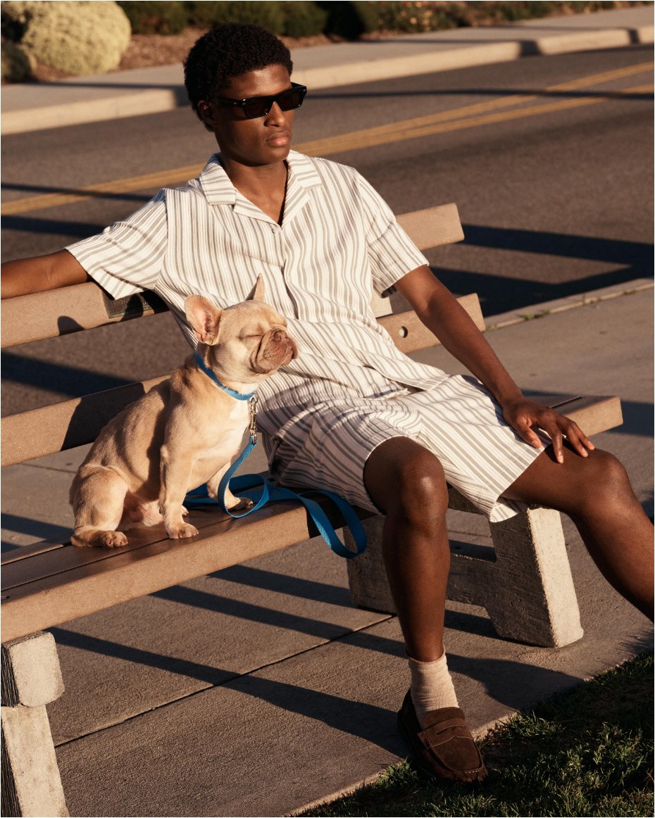 A man sitting on a park bench in a striped short sleeve top & matching shorts.