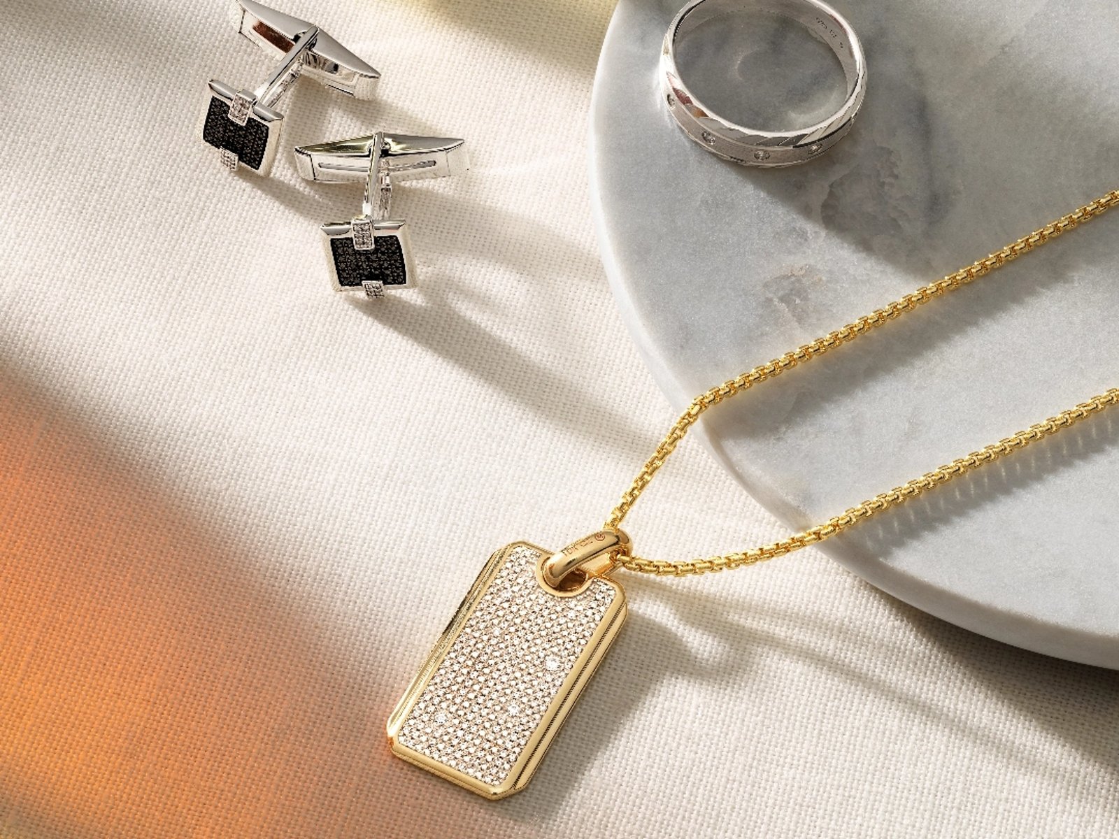 1 photo, of a pair of square silver cuff links, a flat silver band, and a yellow gold and diamond dog tag pendant and chain.
