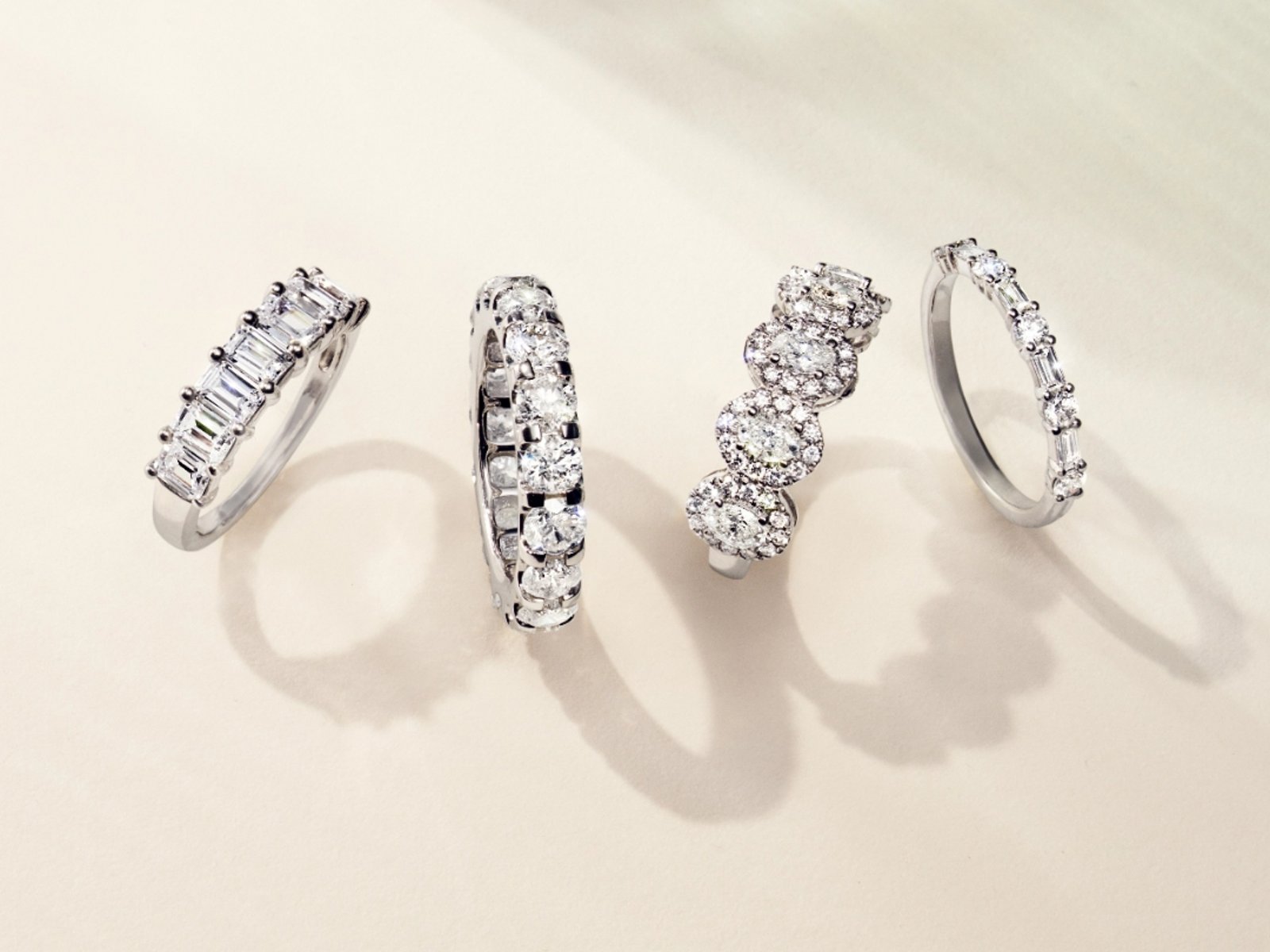 1 photo, of 4 sparkling diamond engagement bands on a cream background, their shadows visible