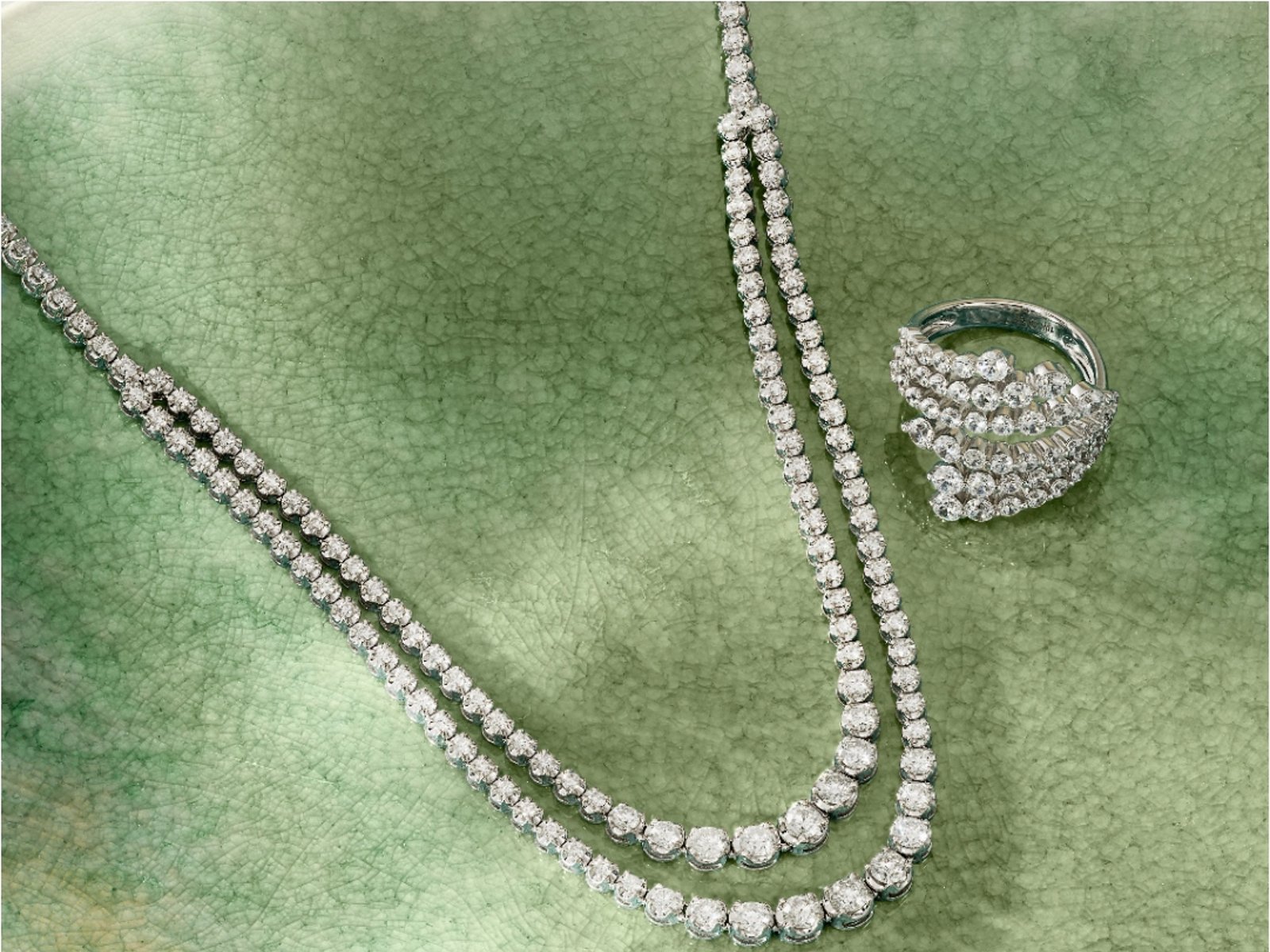 1 photo, of a sparkling two-tier diamond tennis necklace and a bypass diamond ring on a mottled green background.