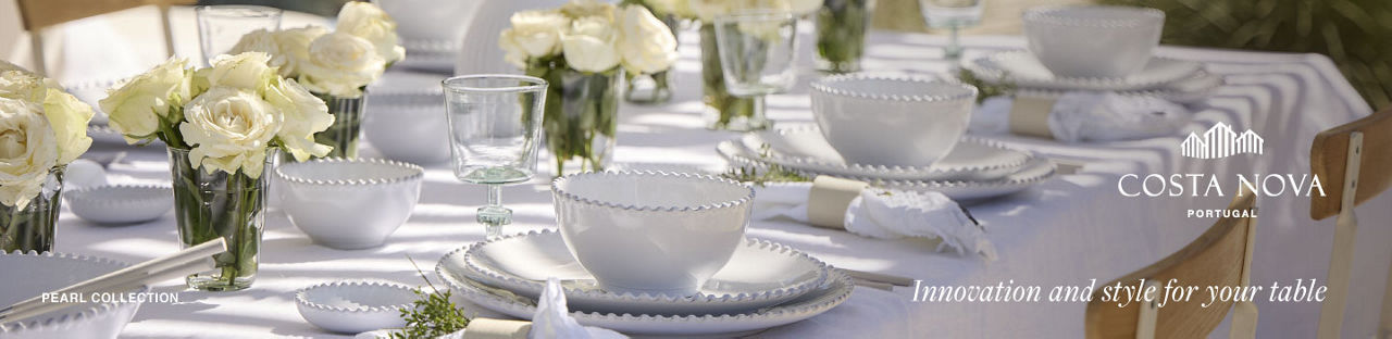 A table outdoors set with white linen, Costa Nova white place settings, and jars of white roses.