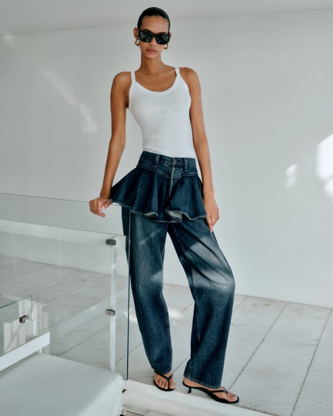 Woman in an Agolde white tank top and blue jeans with skirt element.