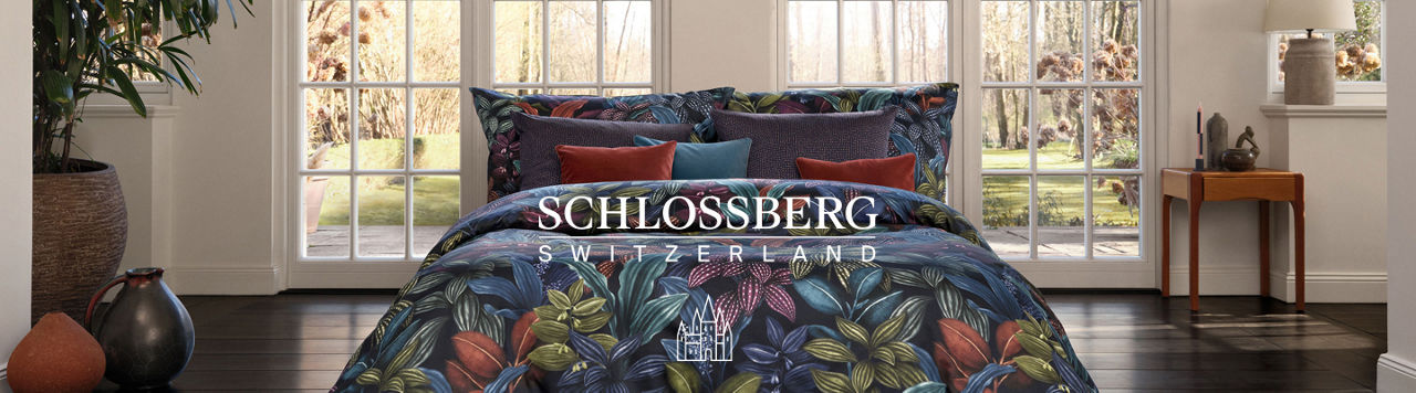 Schlossberg Switzerland. A bed in front of two sets of French doors, made up with vibrantly colored tropical flowers Schlossberg linens.