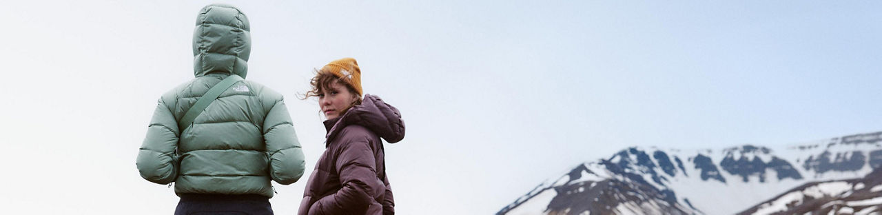 2 women in North Face puffer jackets, a snow covered mountain behind them.