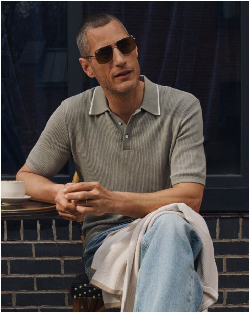 A man sitting with his legs crossed in a light green polo and jeans.